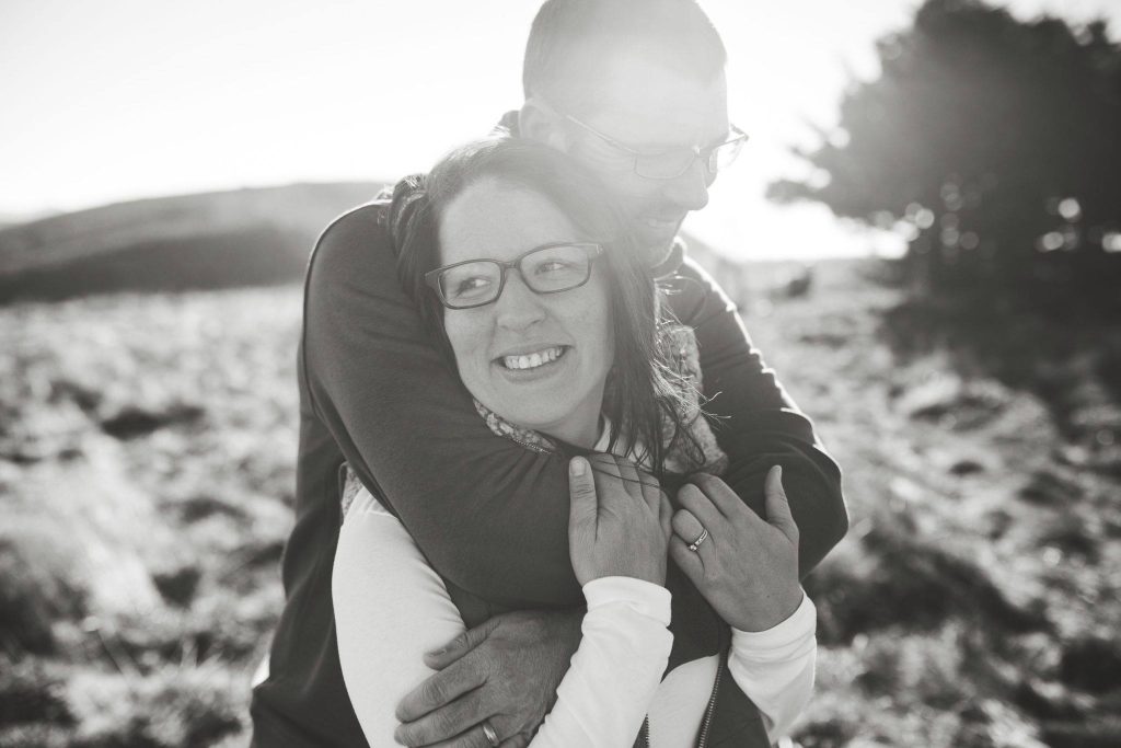 Black and white photo of man holding a woman with the sun shining behind them.