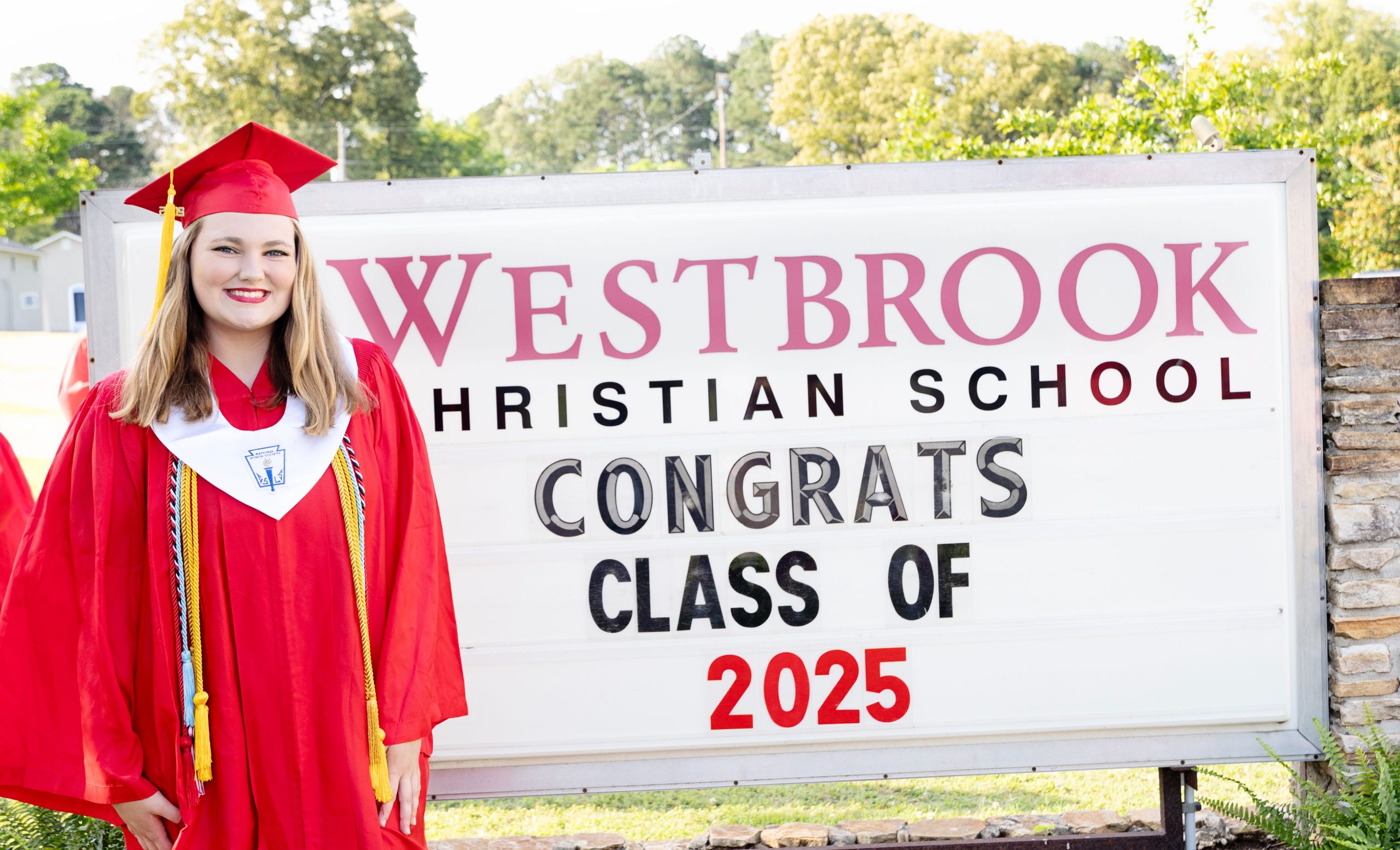 Chelsea Galfas in her graduation gown in front of Westbrook Christian School sign