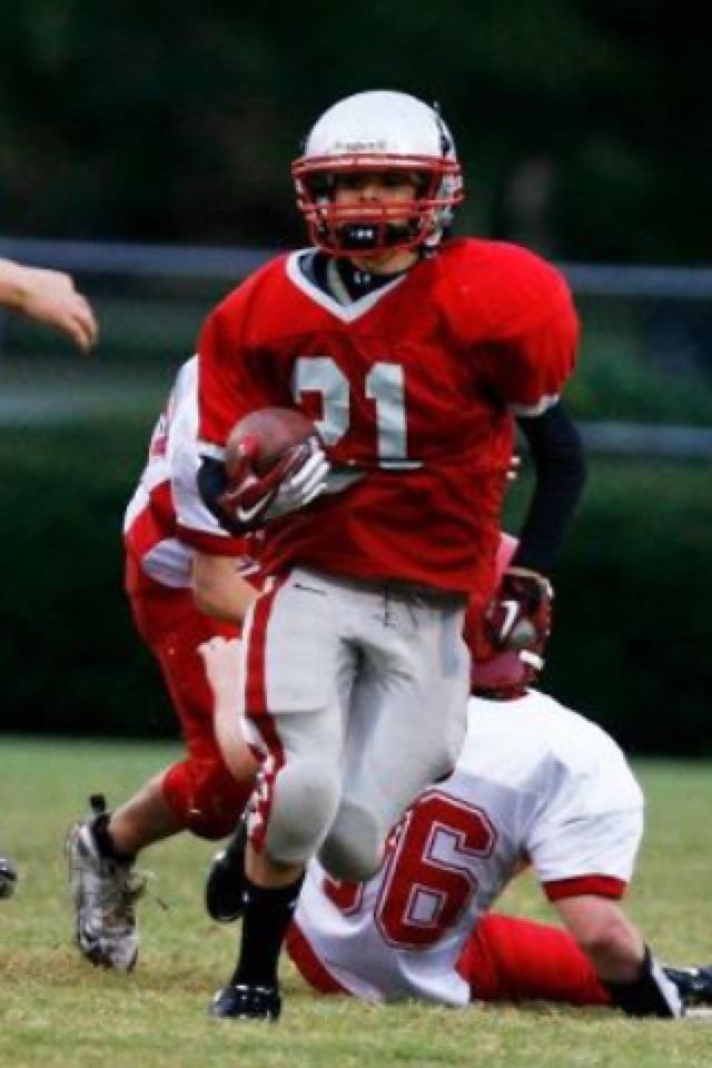 Gilbert runs with the football tucked under his arm as a player in white falls behind him.