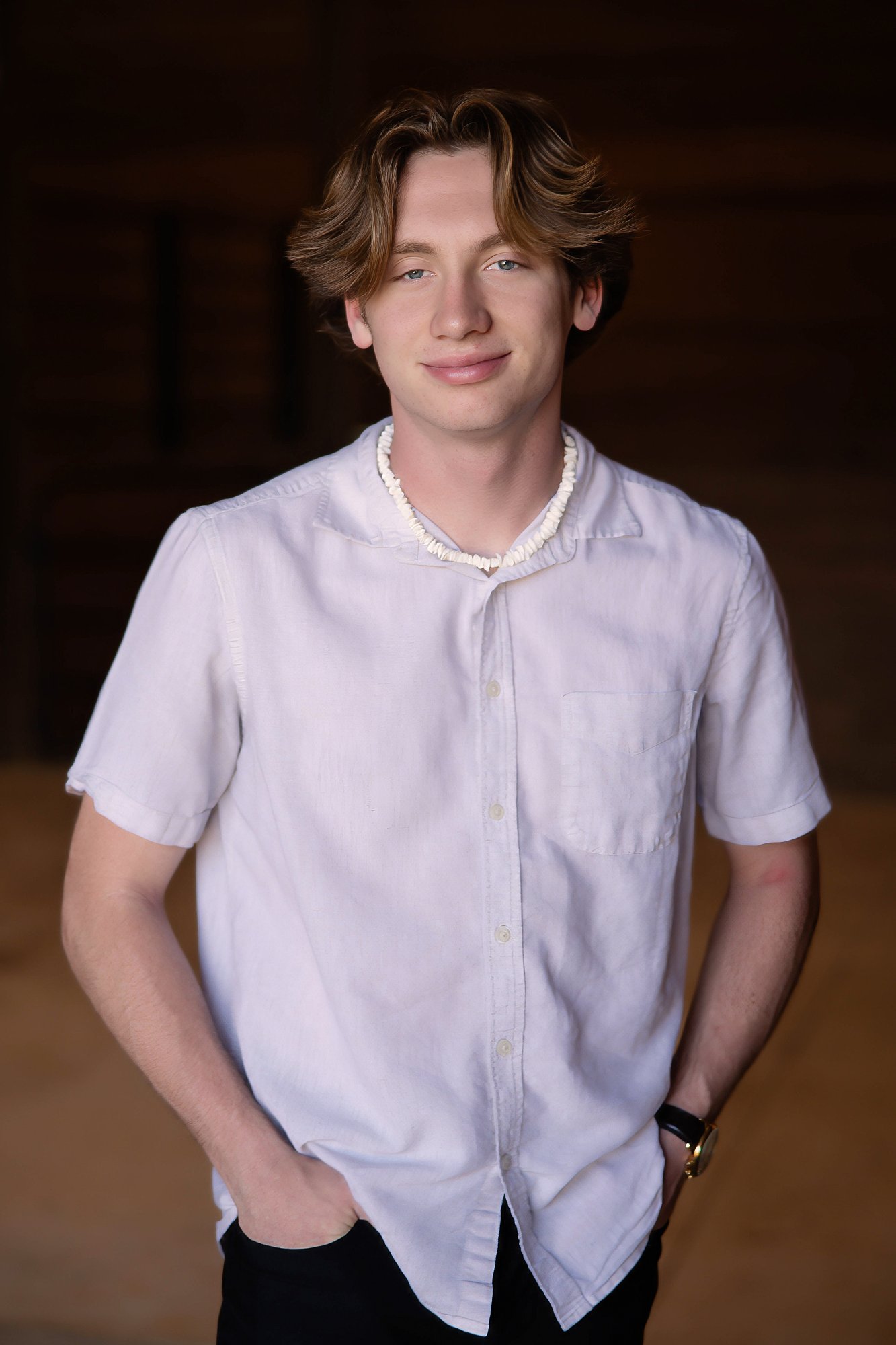 AJ, 18, smiles in a white button-up shirt against a dark background.