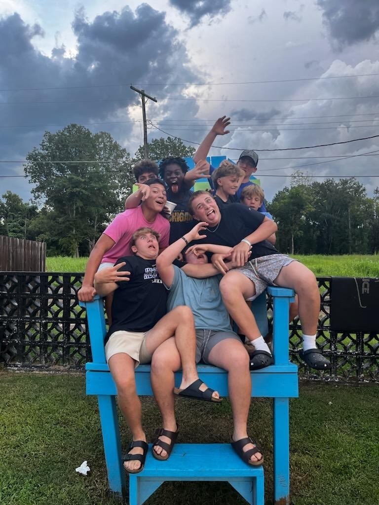 A pile of laughing Boys' Ranch boys crowd onto an oversized blue wooden chair.