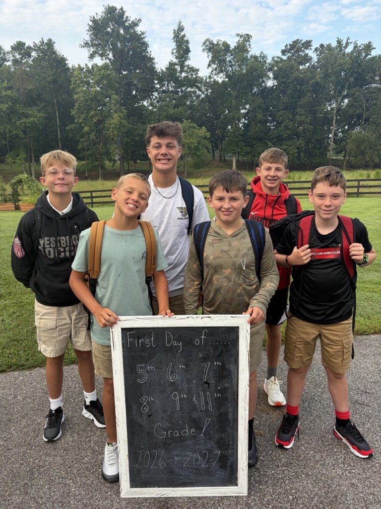 Six Boys' Ranch boys with backpacks hold a chalkboard sign for the first day of school.