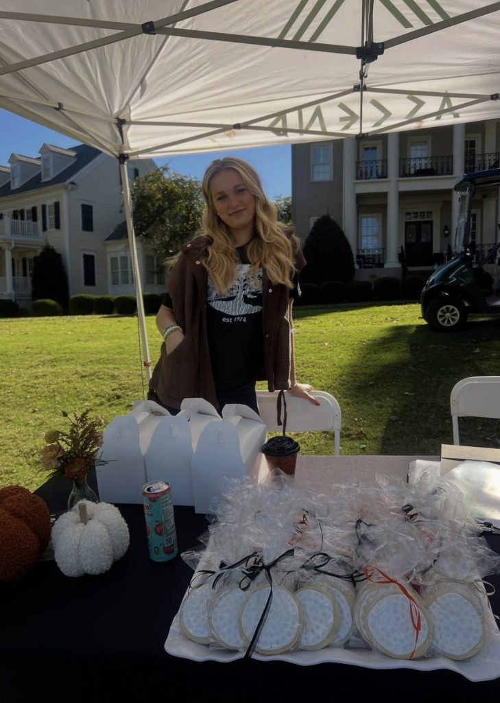 Taylor stands at an outdoor booth under a white tent with her baked goods.