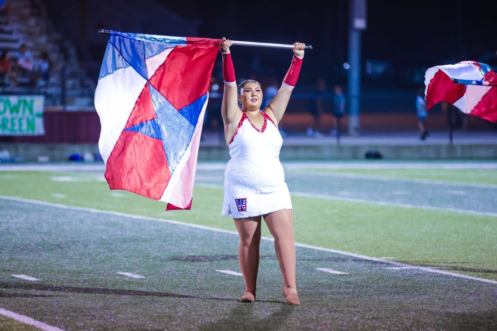 A color guard member in white raises a red, white and blue flag high on the field.