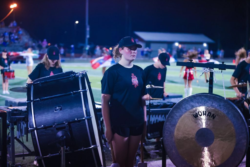 A Westbrook band member stands among the drums and gong on the sideline at night.