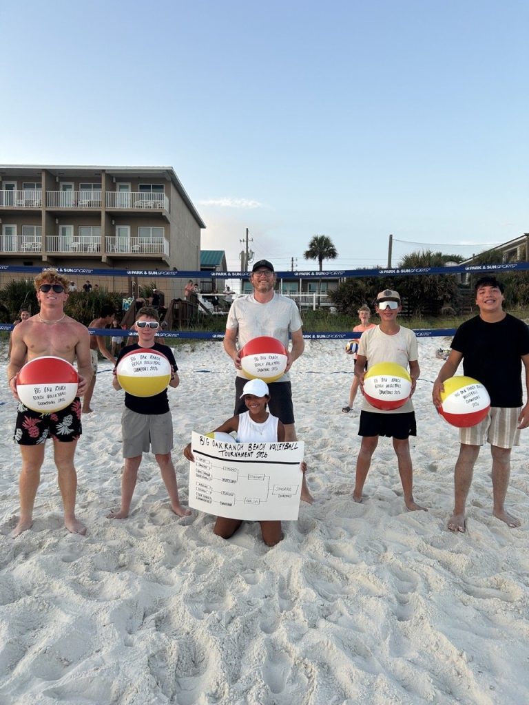 The volleyball tournament champions hold signed beach balls on the sand during the beach trip.