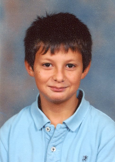 Gilbert as a young boy, smiling in a light blue shirt for a school portrait.