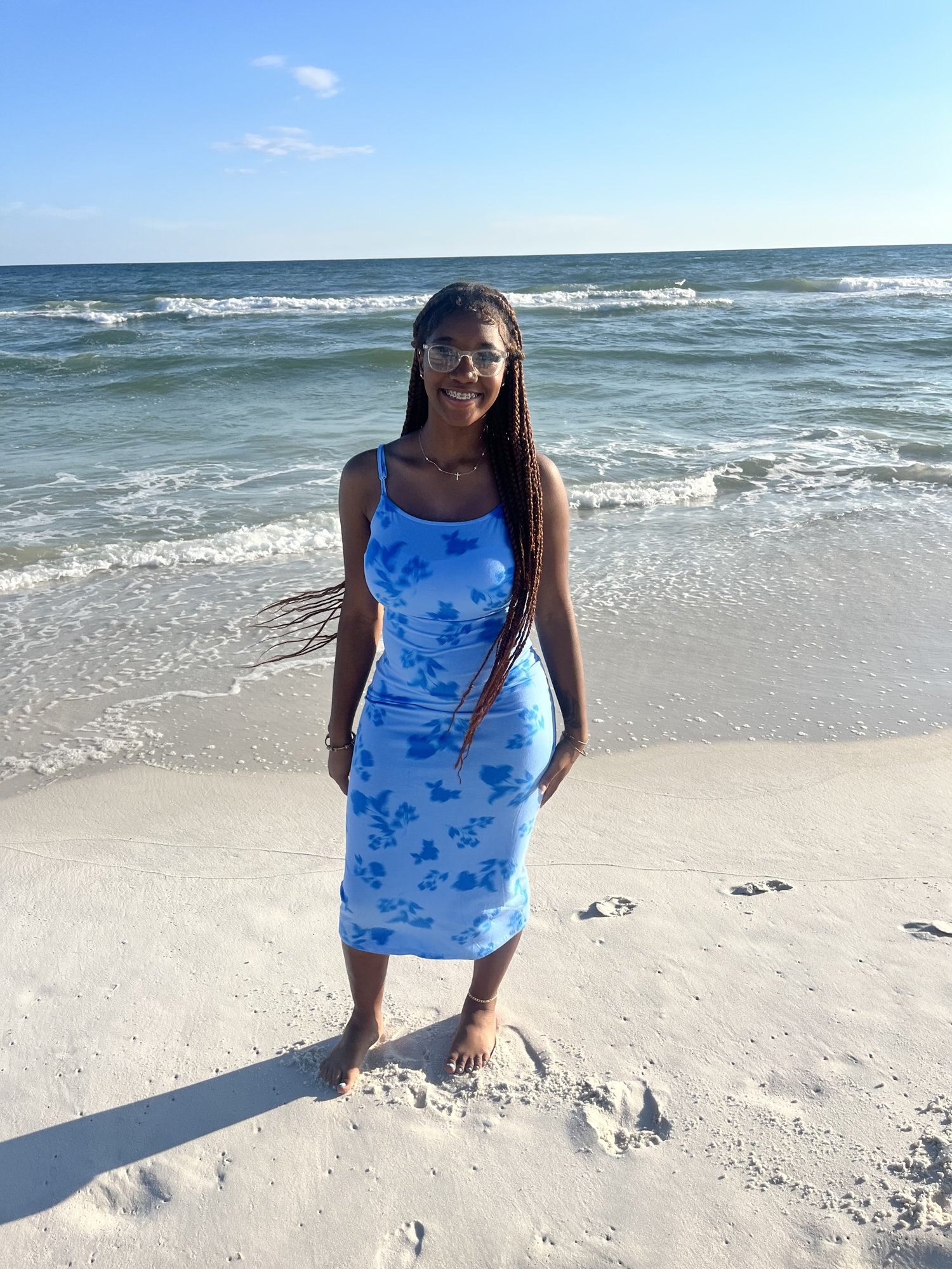 Yanna, 18, smiles on the beach in a blue sundress with the ocean behind her.