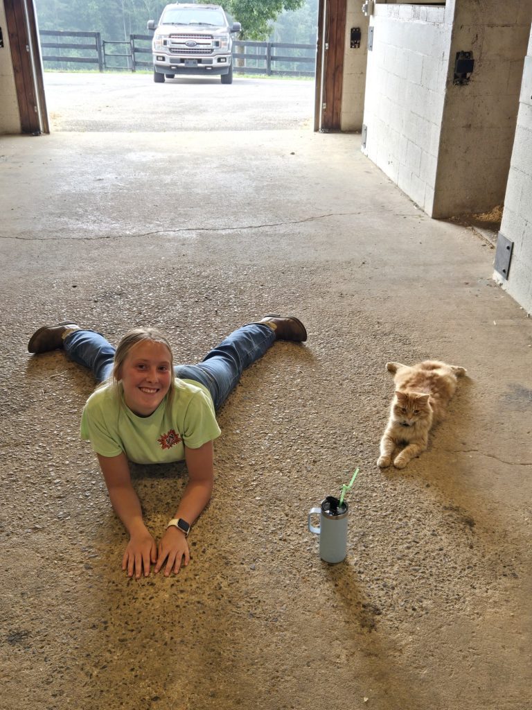 A smiling Girls' Ranch girl lies stretched out on the ground beside a cat.