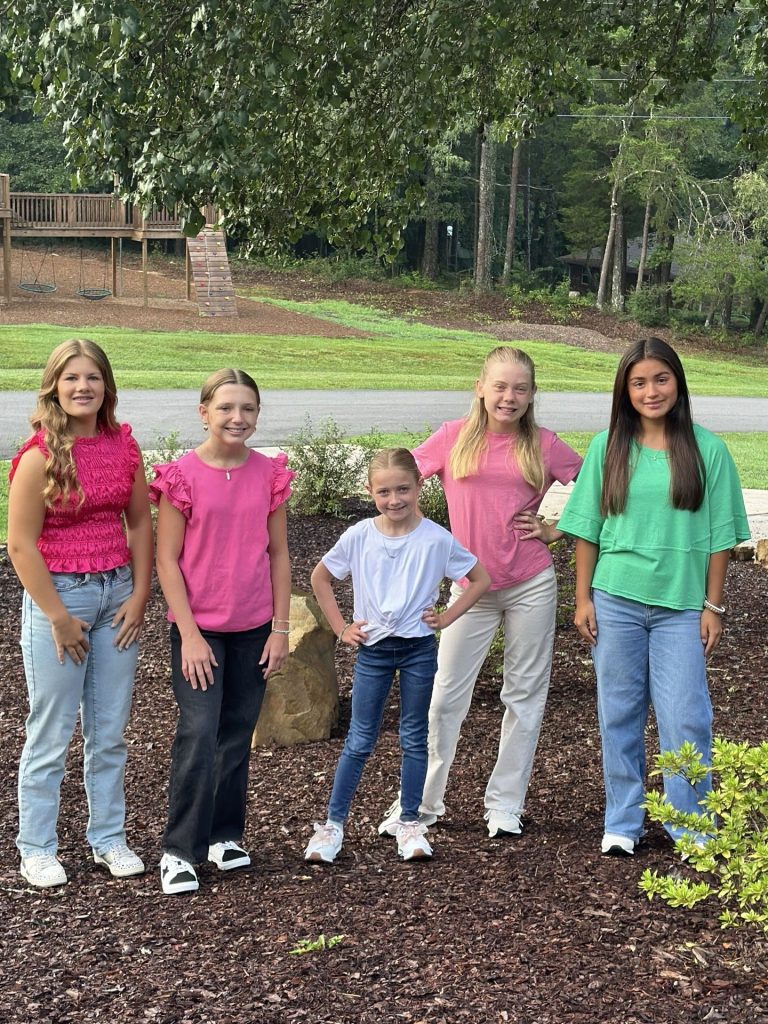 Five Girls' Ranch girls in pink, white and green tops pose together outside.